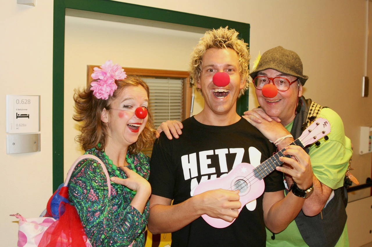 Sascha Grammel steht zwischen zwei Clowns mit einer Ukulele in der Hand un einer roten Nase