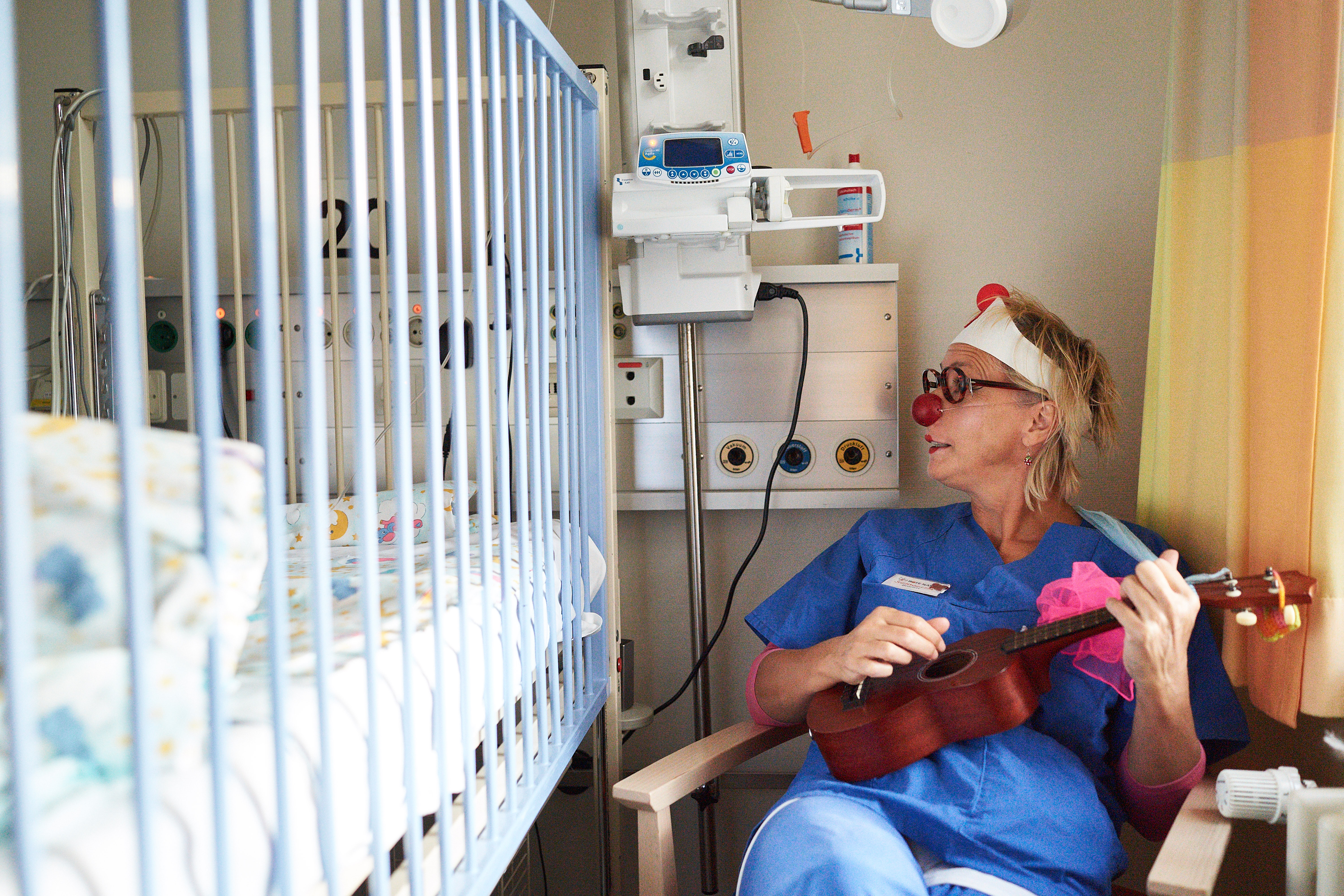 ein Clown mit einer Ukulele sitzt auf einem Stuhl in einem Krankenhaus
