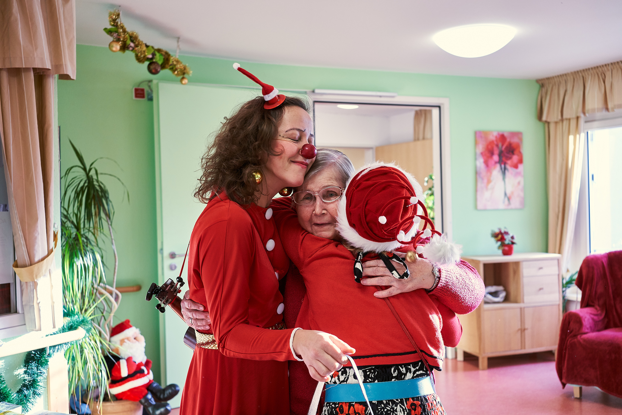 Zwei Clowns umarmen im Weinachts Kostüm eine ältere Frau 