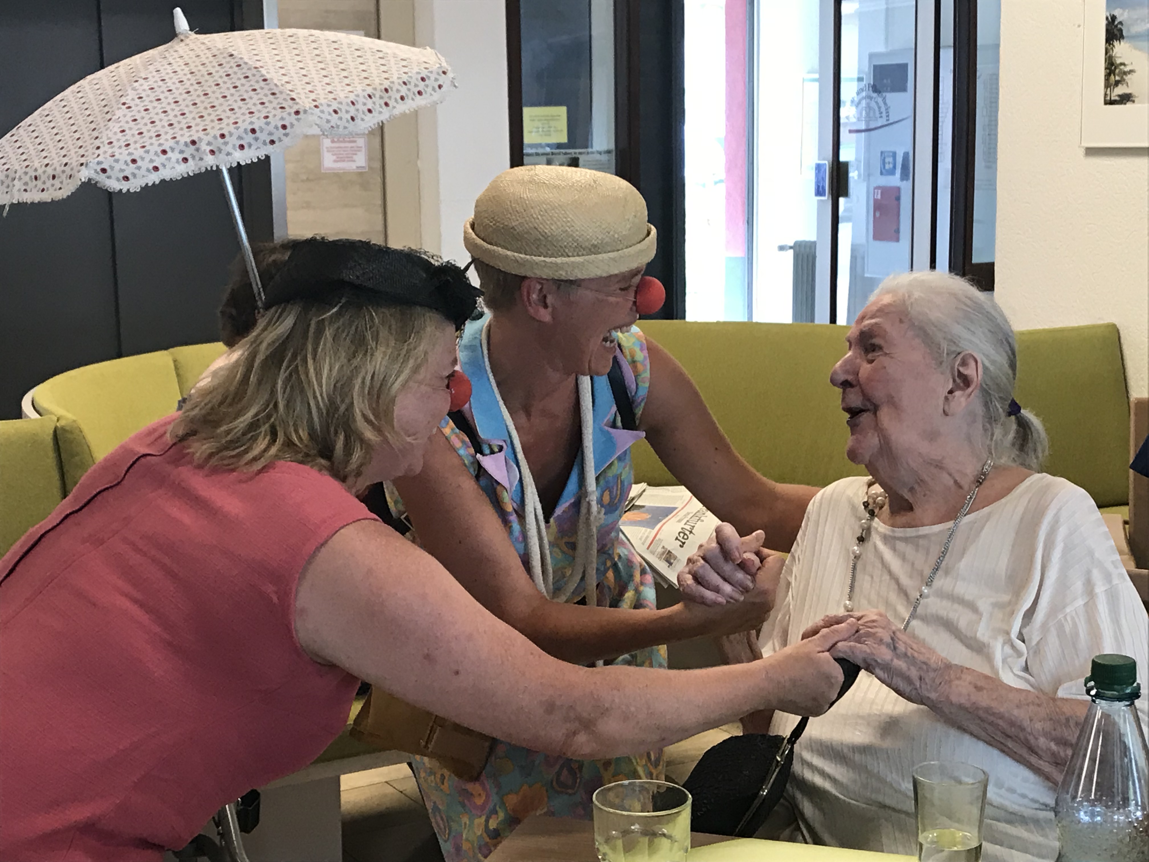 Zwei Clowns beugen sich u einer älteren Dame runter um mit ihr zu reden