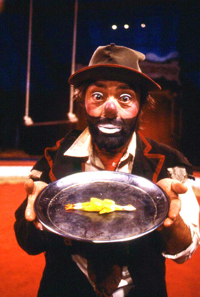 Ein Clown der einen Teller mit etwas drauf in die Kamara hält 