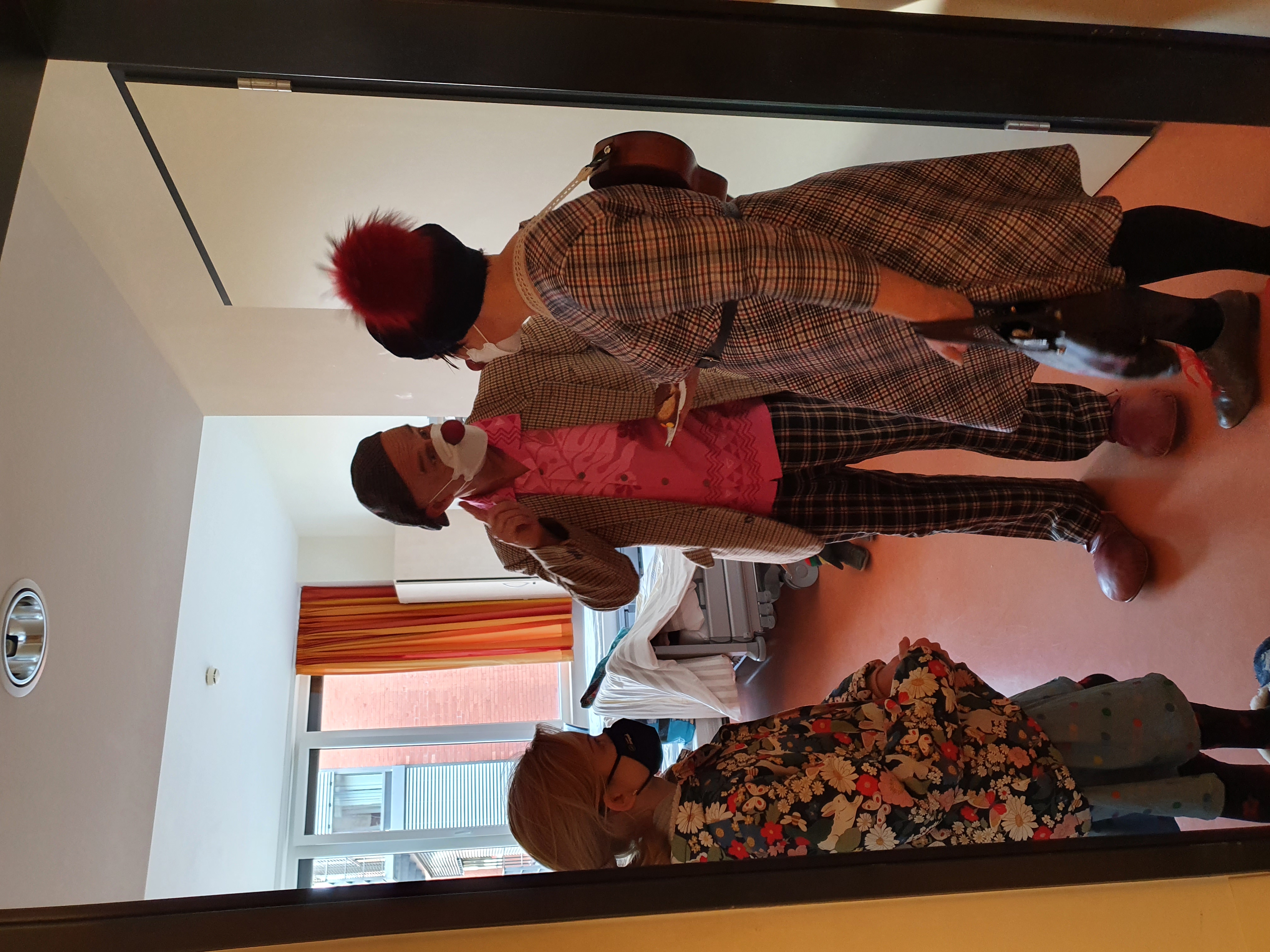 2 Clowns stehen im Zimmer mit einer Patientin und essen Kuchen