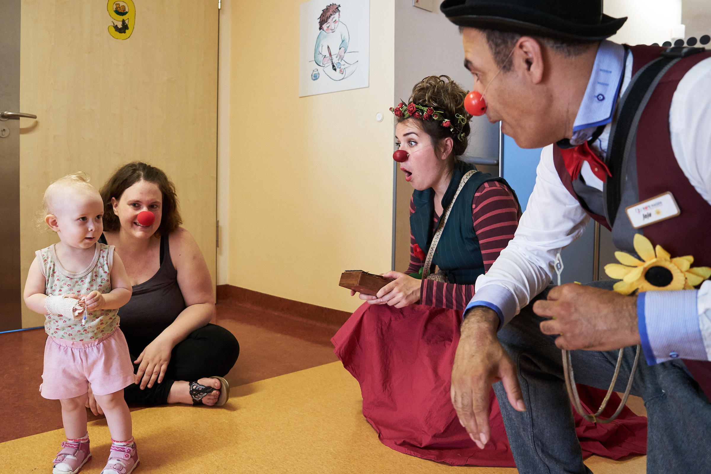 Zwei Clowns hocken vor einem kleinem Kind mit seiner Mutter 