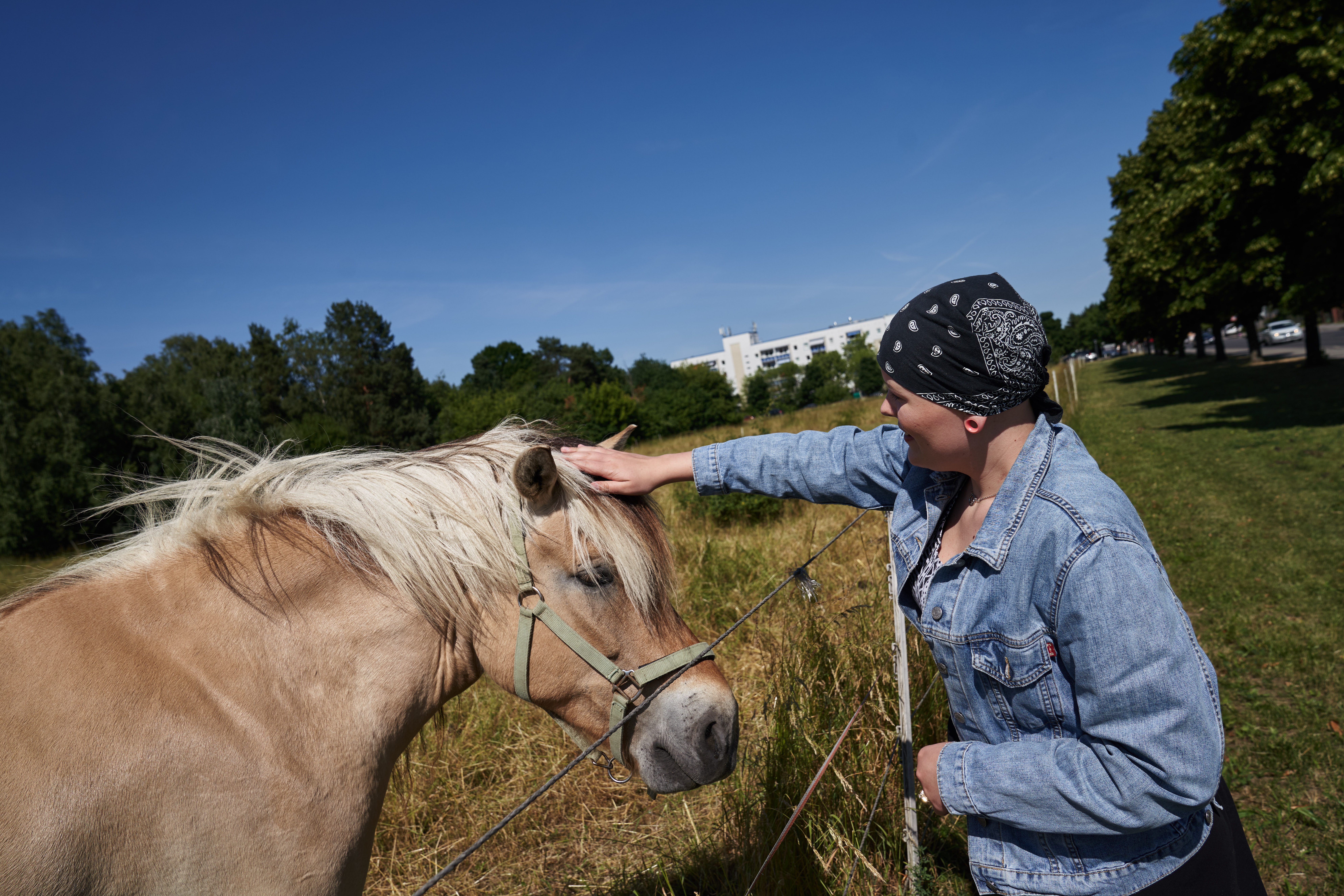 Michelle im Kopftuch streichelt ein Pferd auf der Wiese.