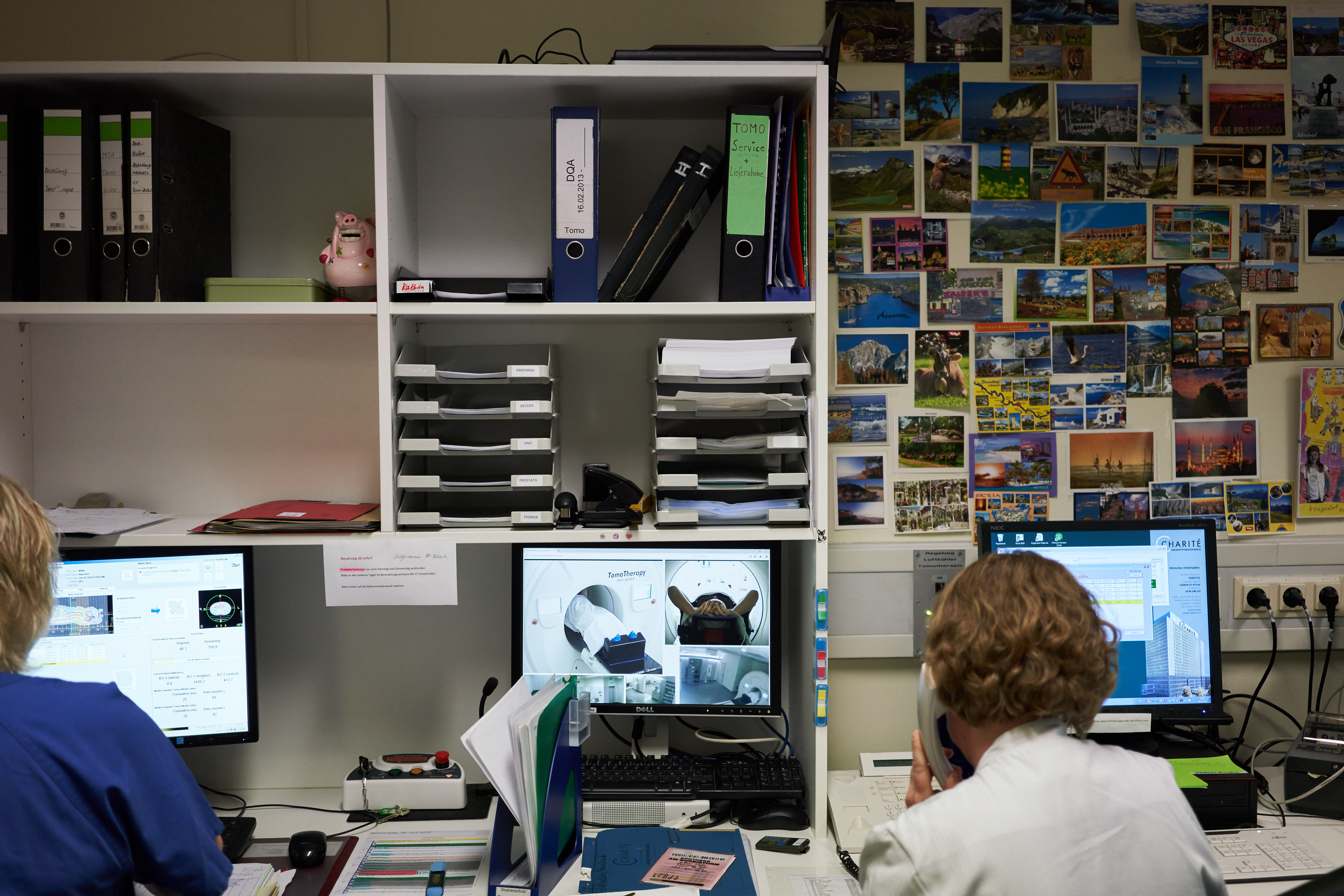 In einem Pflegerinnenzimmer sitzen zwei Pflegekräfte und schauen in Rechner hinein. 
