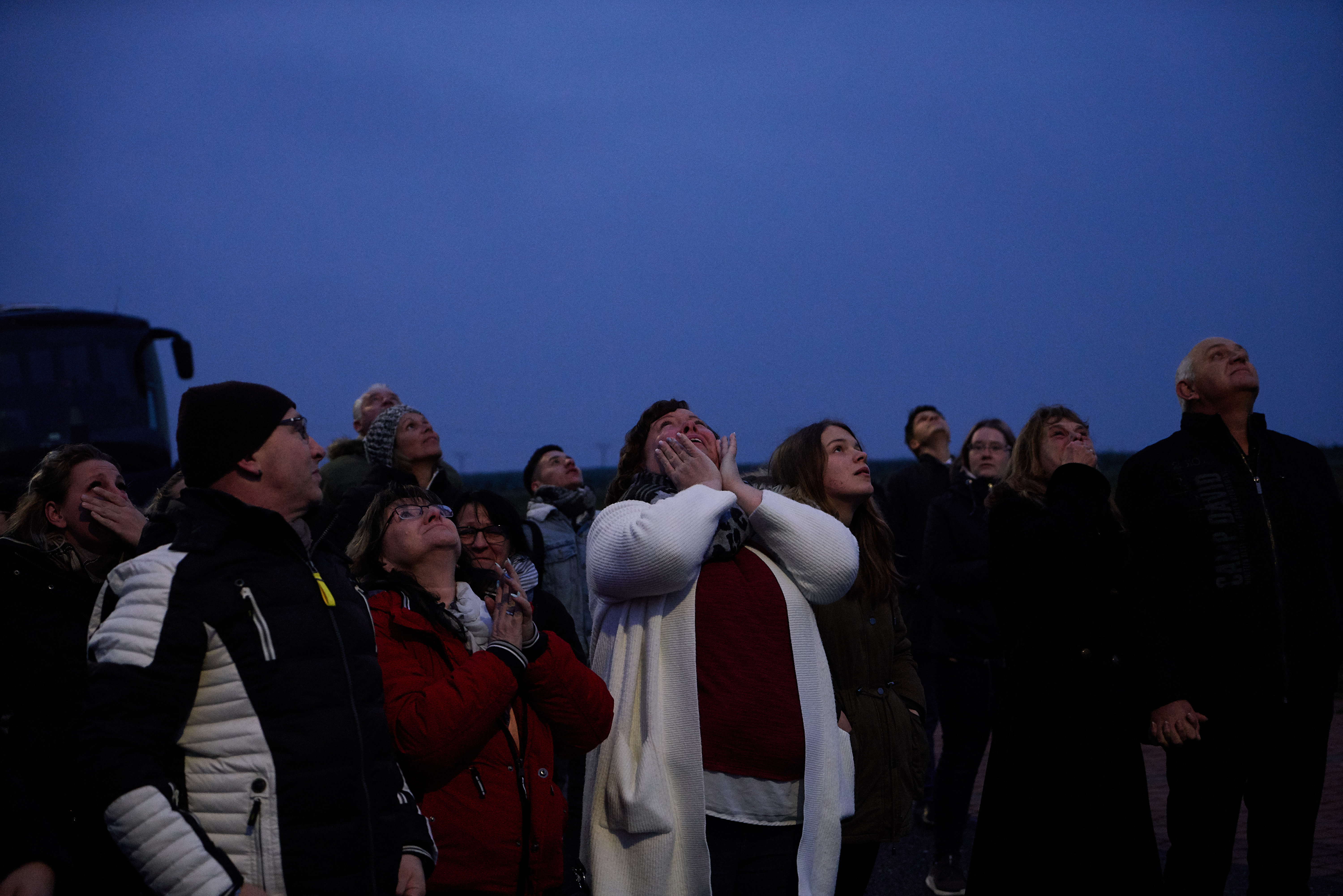 Menschenmeng steht in der Nacht draußen und schaut in den schwarzen Himmel hoch.
