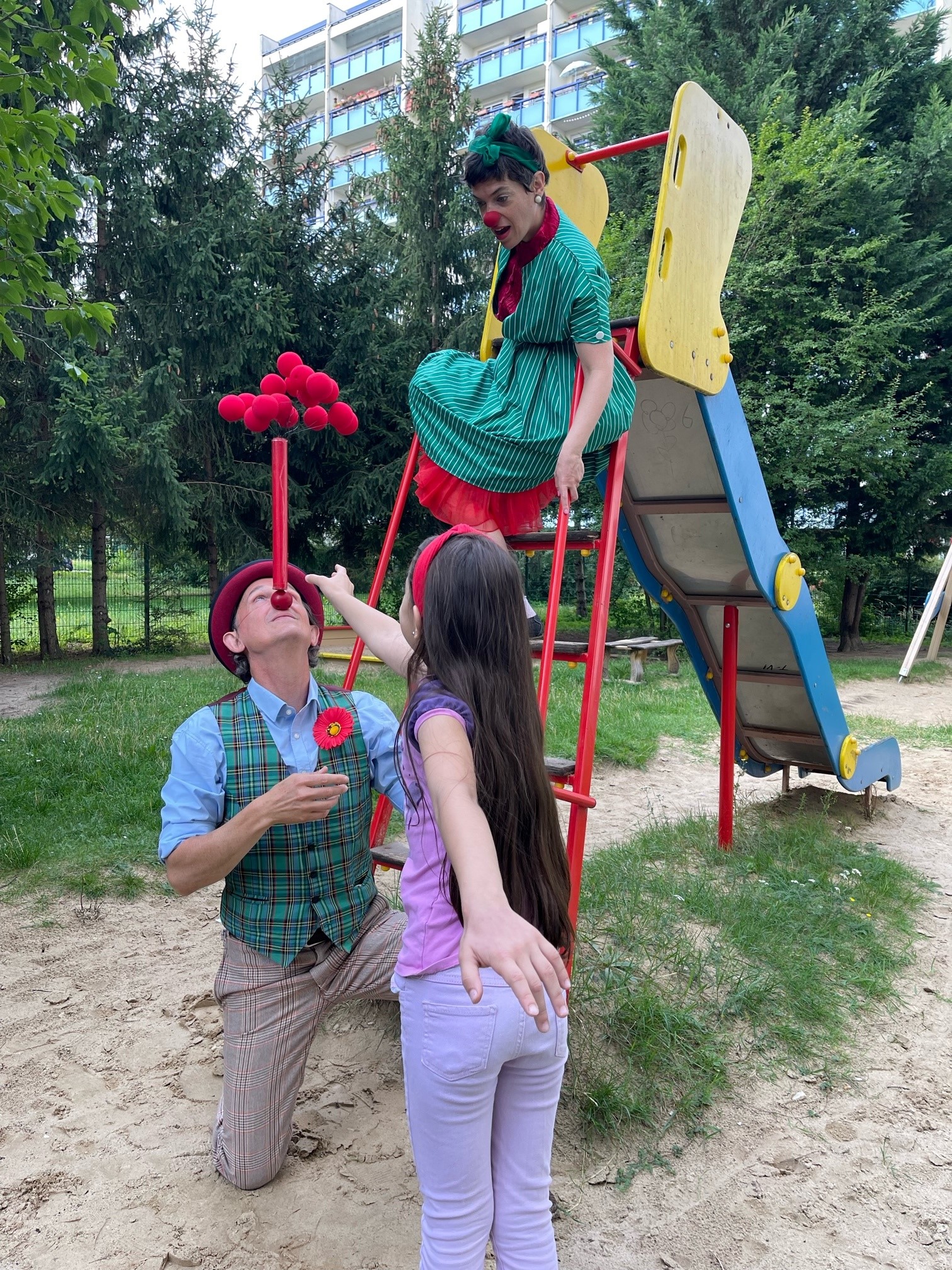 Zwei Clowns spielen mit einem kleinen Mädchen an einer Rutsche