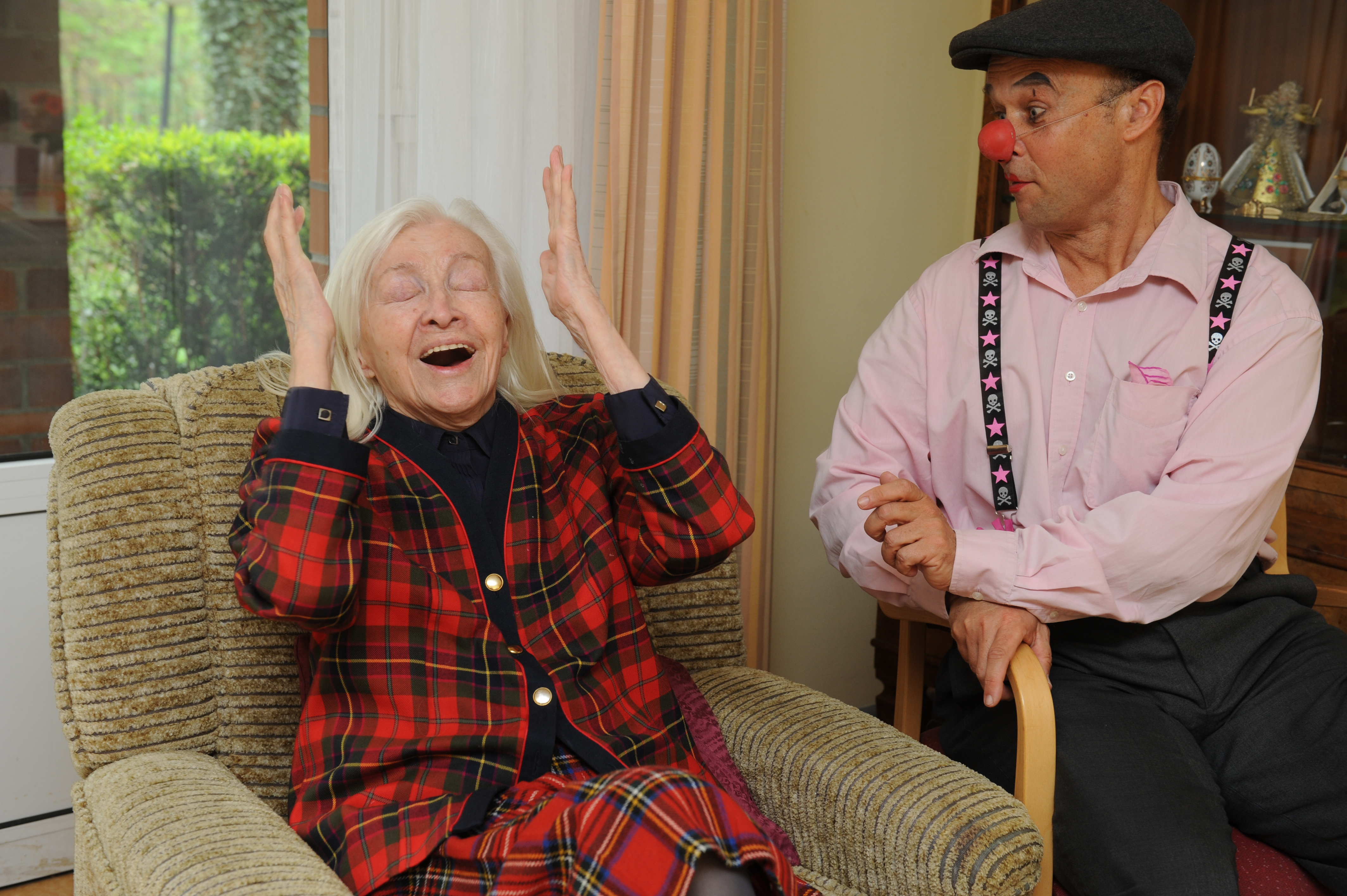 Eine Seniorin hebt aktiv lächelnd die Hände in die Luft. Ein Klinikclown lächelt. Fünf Clowntipps zum kreativen Umgang mit Demenz.