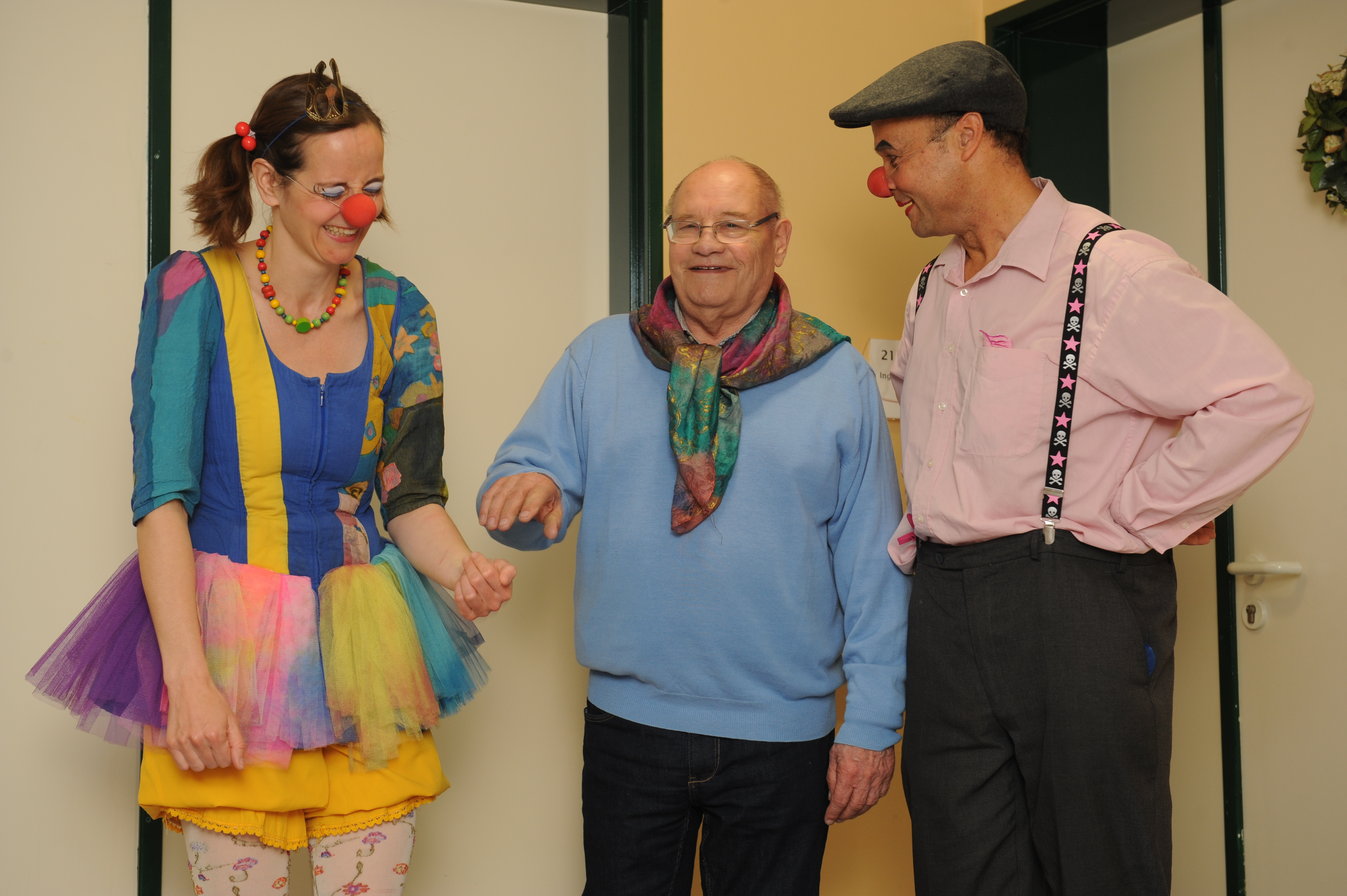 Ein Senior lächelt zwei ROTE NASEN Klinikclowns an. Fünf Clowntipps zum kreativen Umgang mit Demenz.
