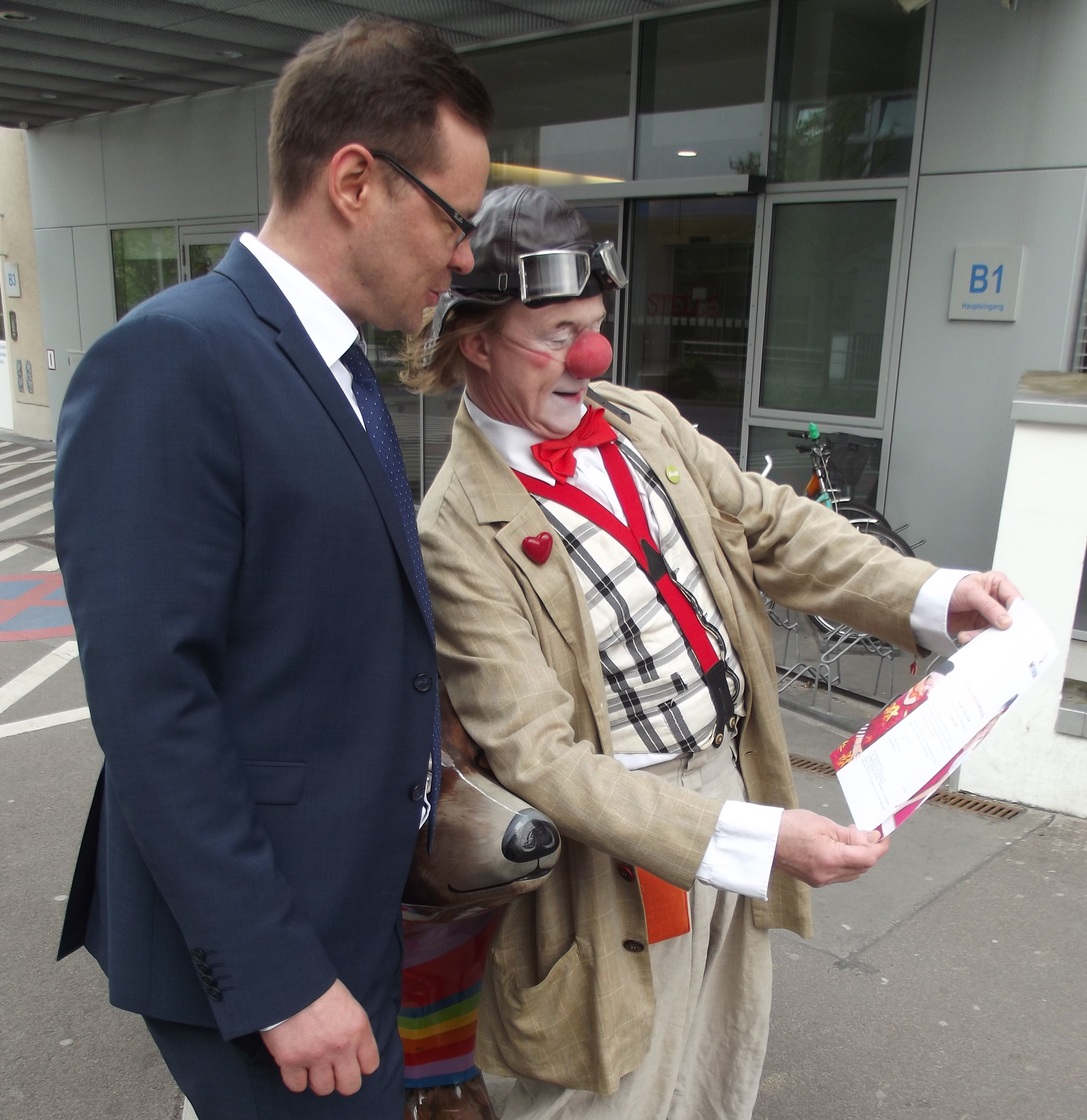 Clown zeigt Manager von Aristo Pharma Urkunde für Patenschaft
